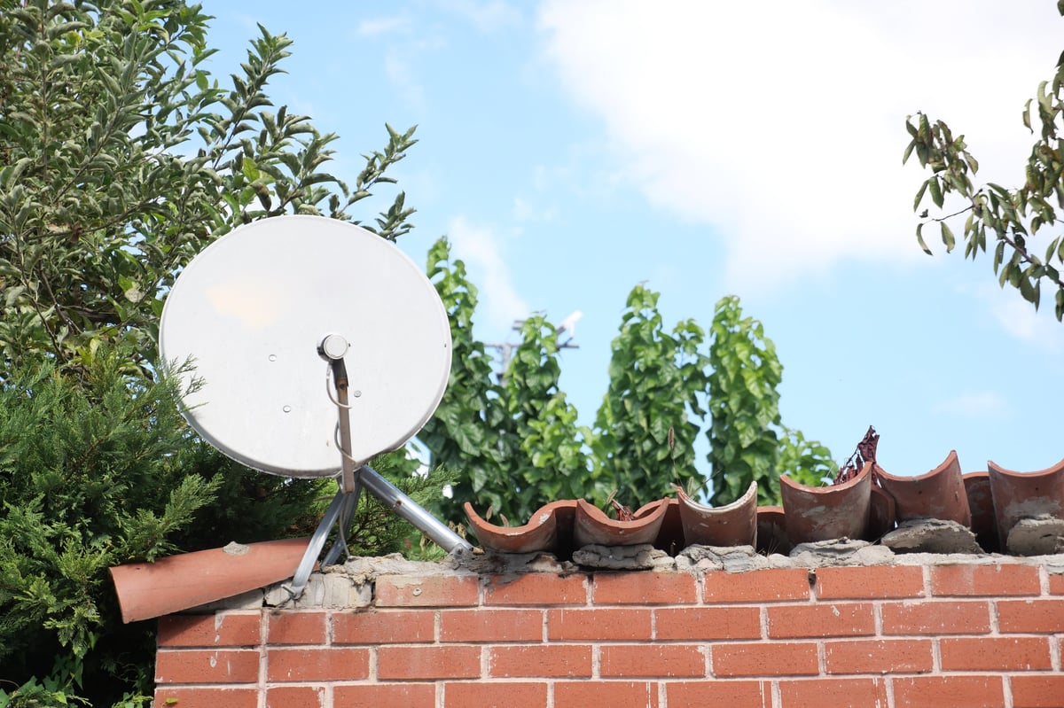 Professional satellite technician installing dish on modern home